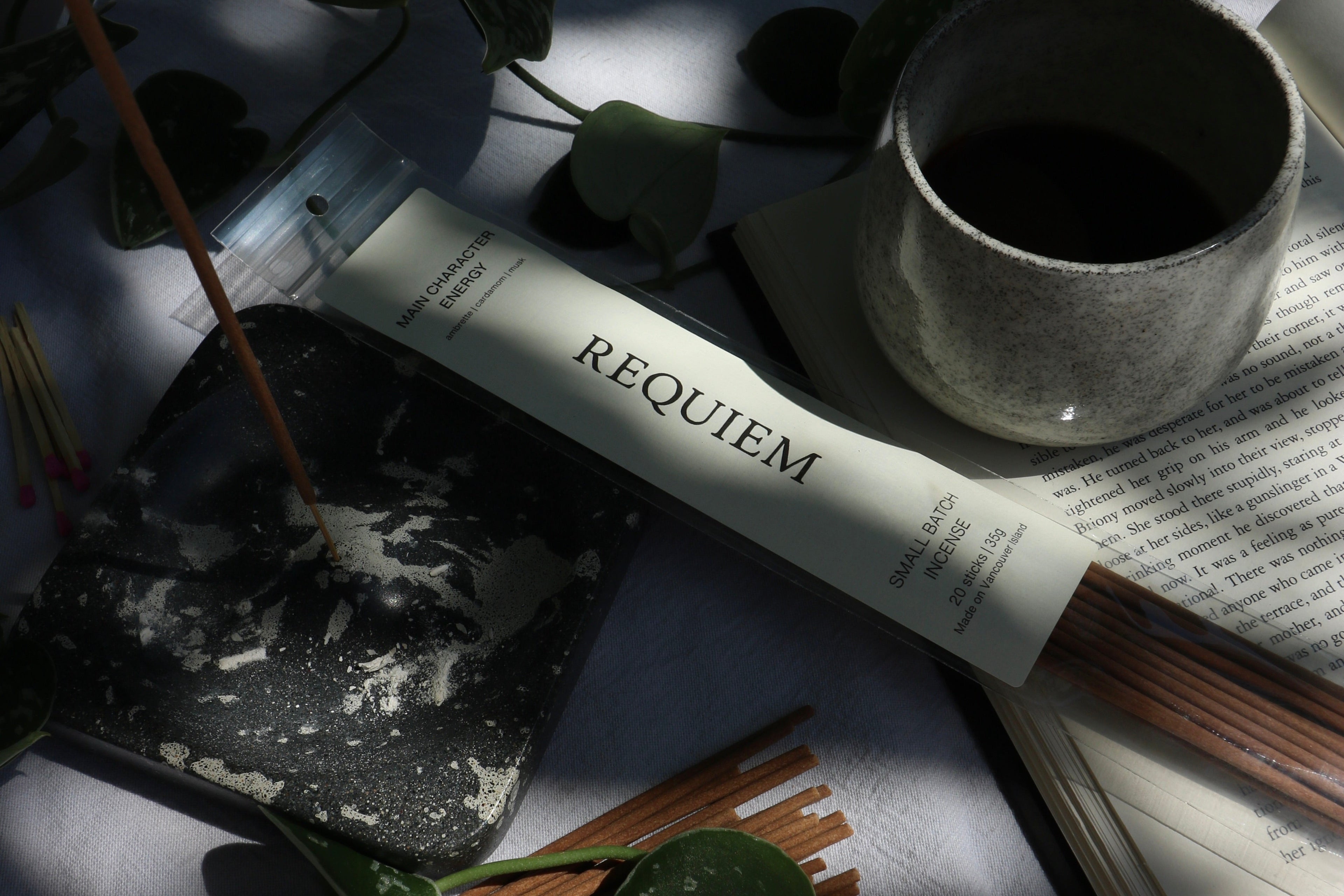 Requiem Incense Company Main Character Energy Incense Sticks flat lay with incense sticks, book, vine, and coffee on grey background
