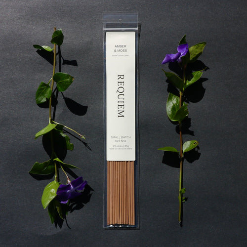 Requiem Incense Company Amber & Moss incense sticks with green leaves and purple flowers on a dark background