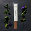 Requiem Incense Company Brewed Awakening incense sticks with green leaves and purple flowers on a dark background
