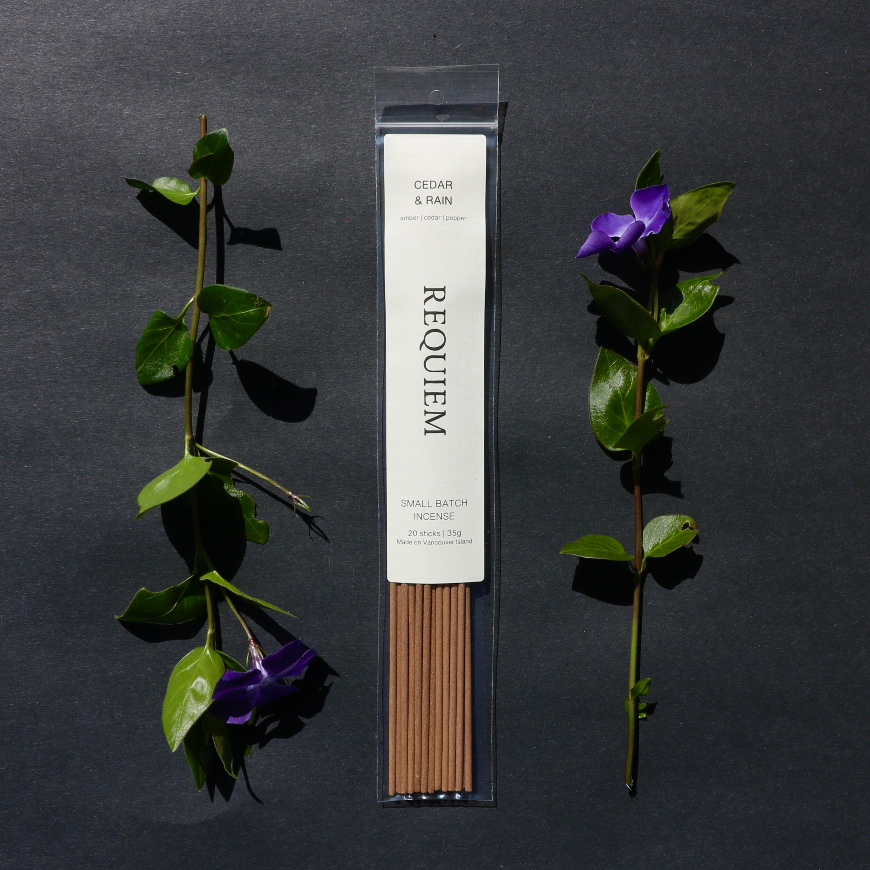 Requiem Incense Company Cedar & Rain incense sticks with green leaves and purple flowers on a dark background