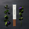 Requiem Incense Company Fireside Solstice incense sticks with green leaves and purple flowers on a dark background