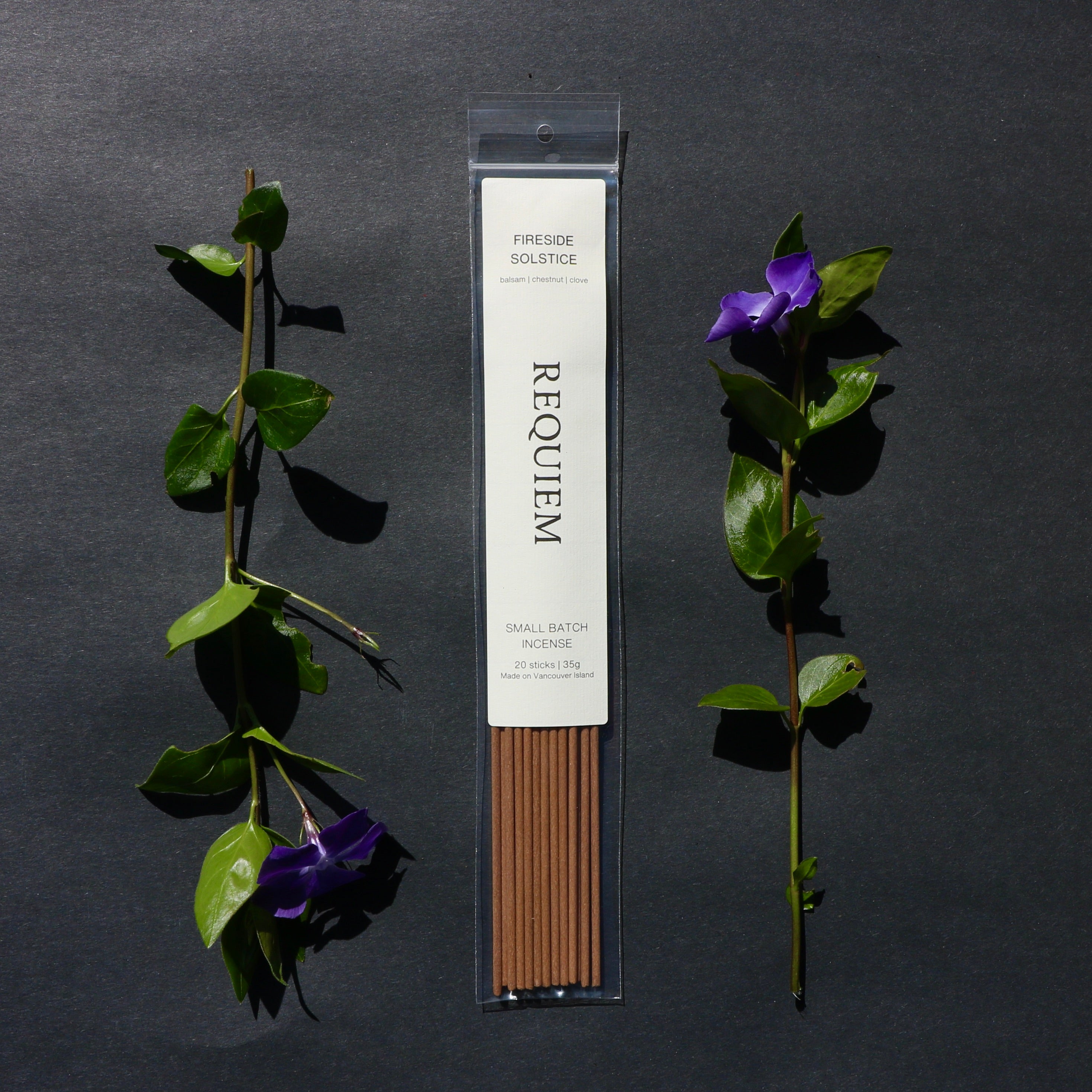 Requiem Incense Company Fireside Solstice incense sticks with green leaves and purple flowers on a dark background