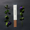 Requiem Incense Company Gingerwood + Palo Santo incense sticks with green leaves and purple flowers on a dark background