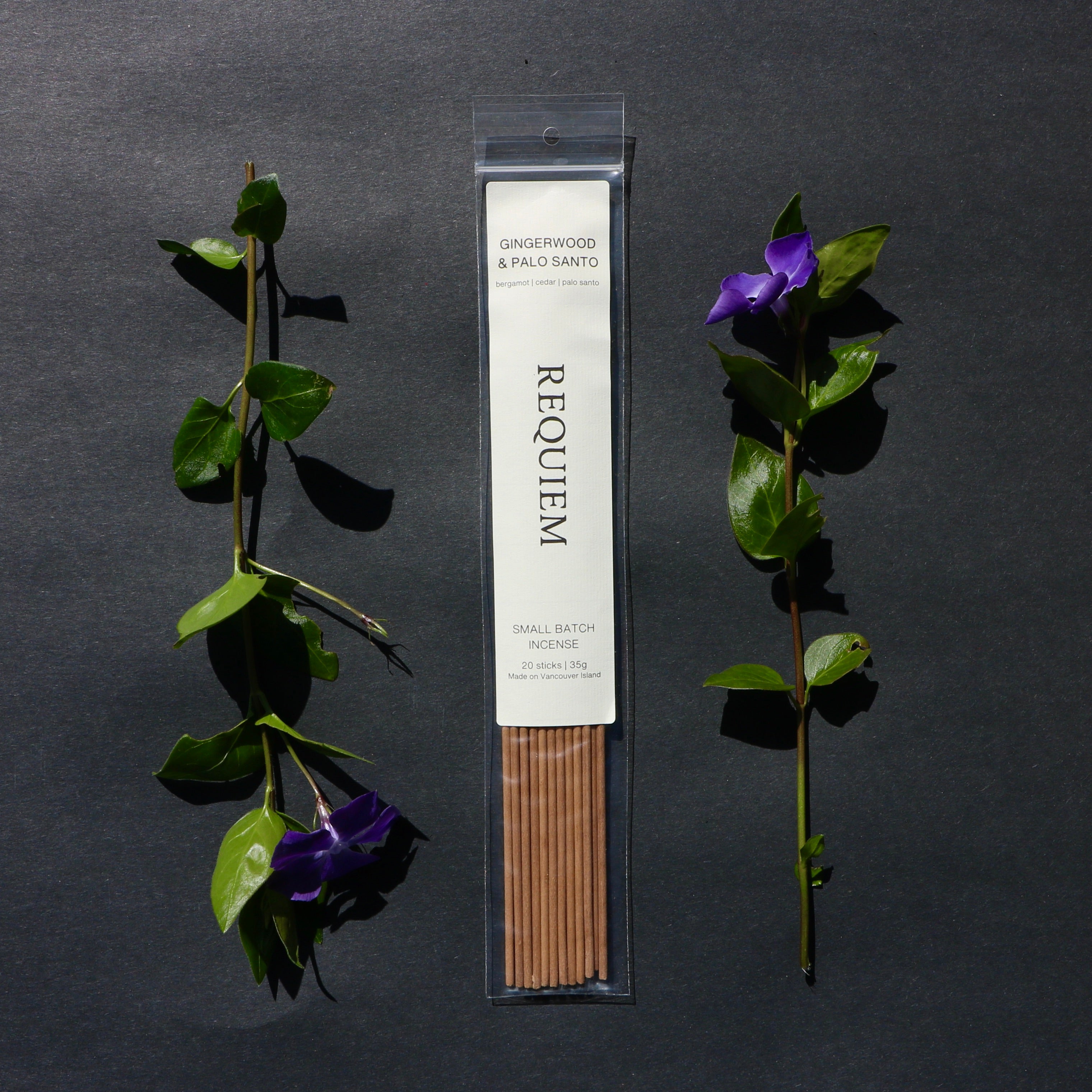Requiem Incense Company Gingerwood + Palo Santo incense sticks with green leaves and purple flowers on a dark background