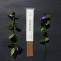 Requiem Incense Company Purple Haze incense sticks with green leaves and purple flowers on a dark background