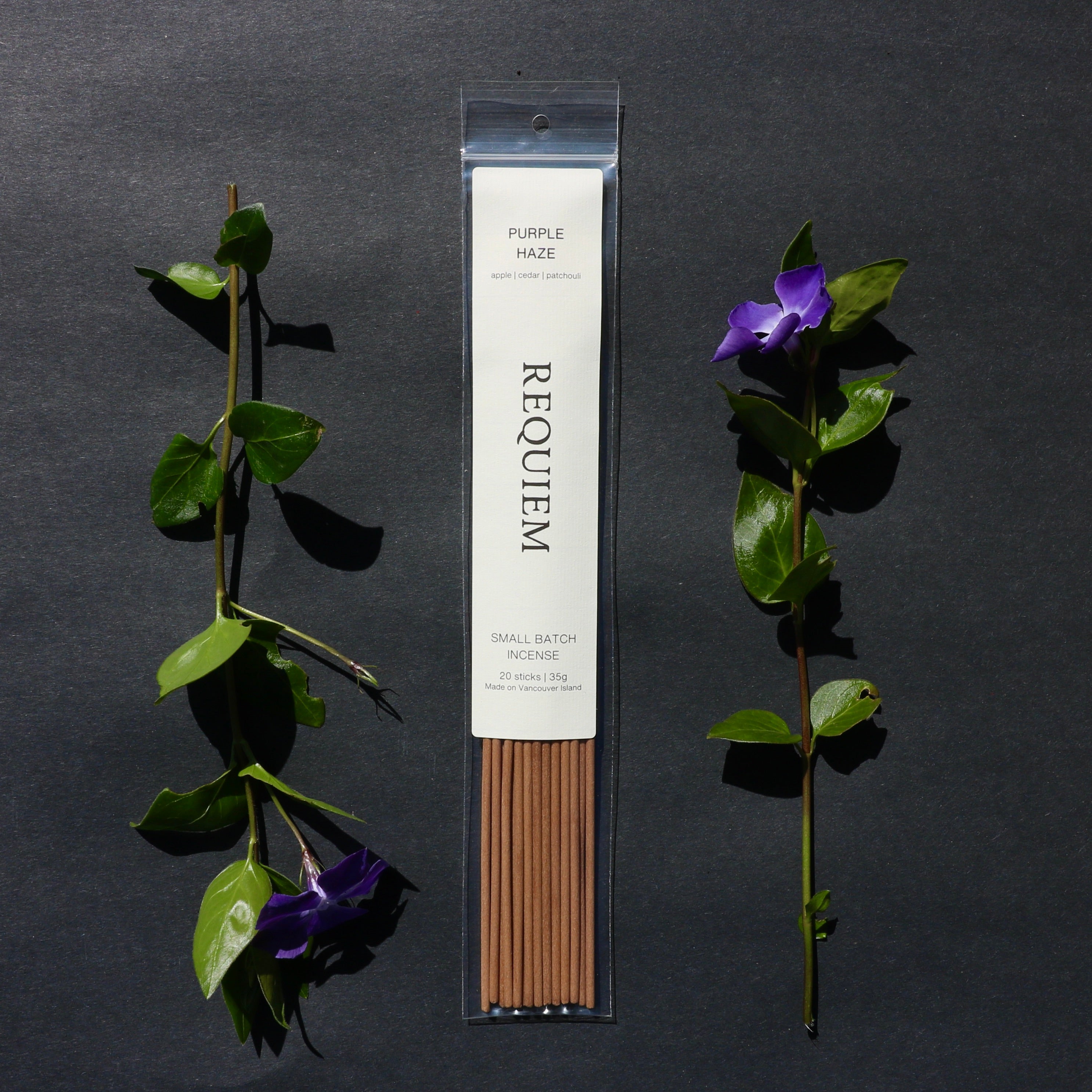 Requiem Incense Company Purple Haze incense sticks with green leaves and purple flowers on a dark background