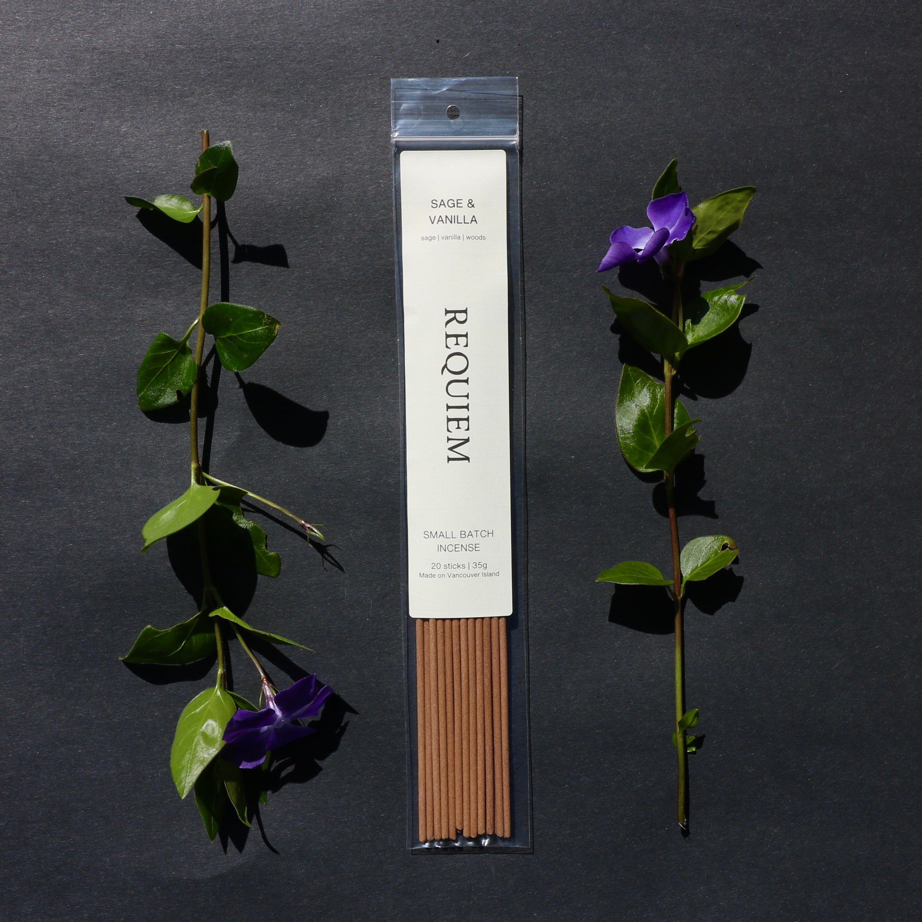 Requiem Incense Company Sage & Vanilla incense sticks with green leaves and purple flowers on a dark background