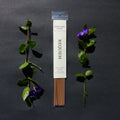 Requiem Incense Company Sandalwood & Spice incense sticks with green leaves and purple flowers on a dark background