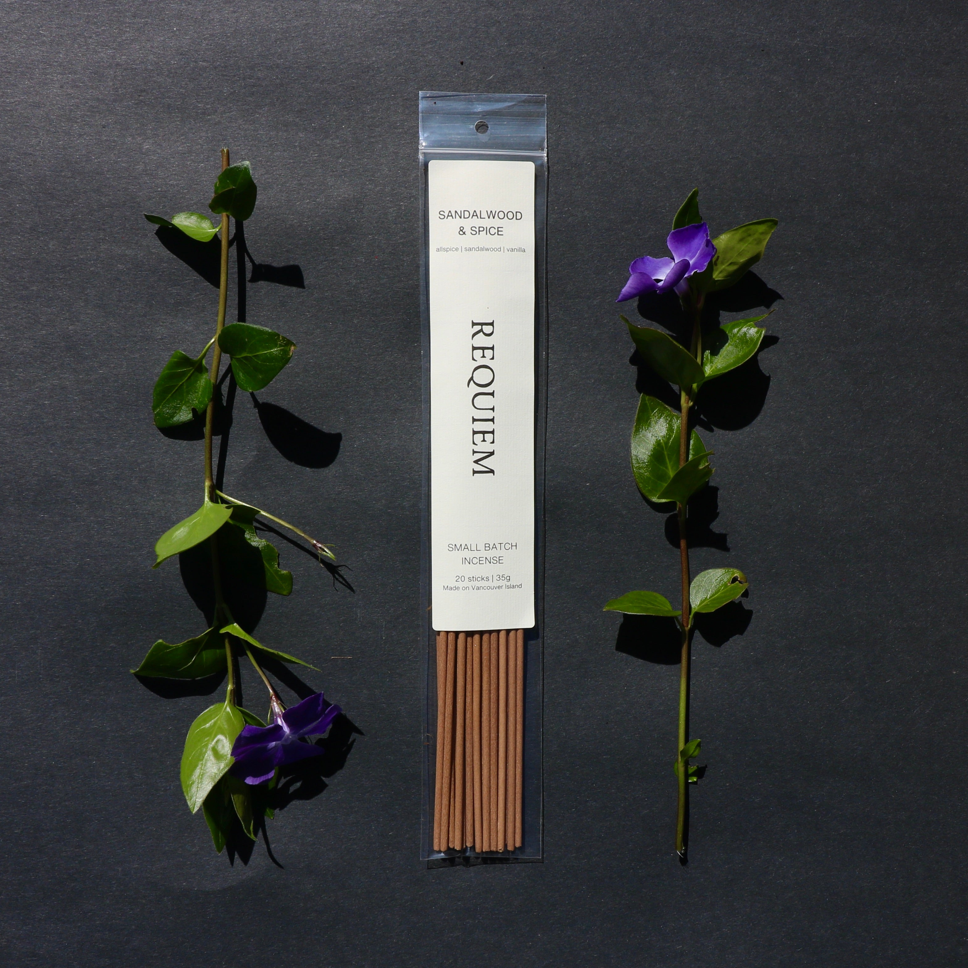 Requiem Incense Company Sandalwood & Spice incense sticks with green leaves and purple flowers on a dark background