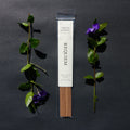 Requiem Incense Company Tobacco & Vanilla incense sticks with green leaves and purple flowers on a dark background