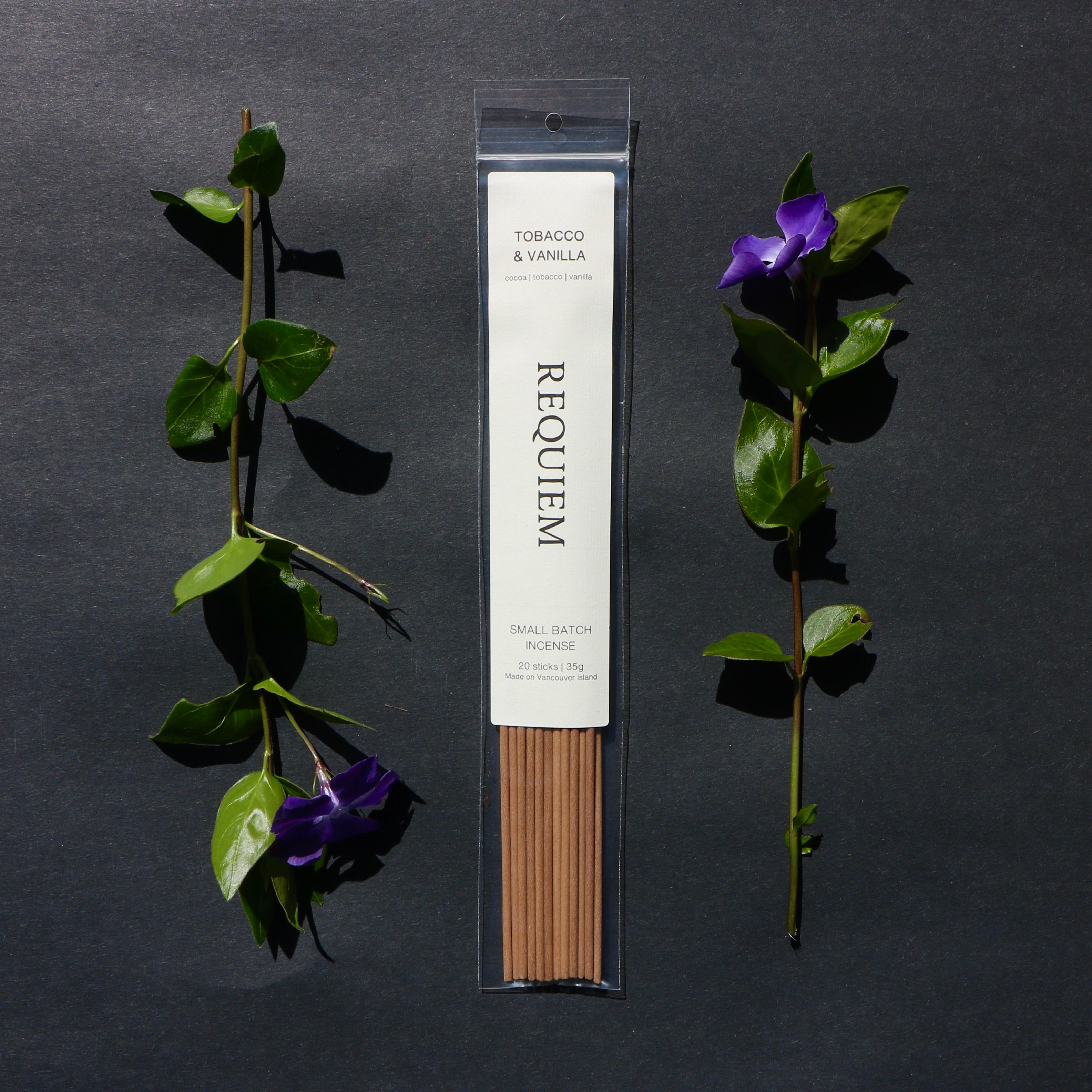 Requiem Incense Company Tobacco & Vanilla incense sticks with green leaves and purple flowers on a dark background