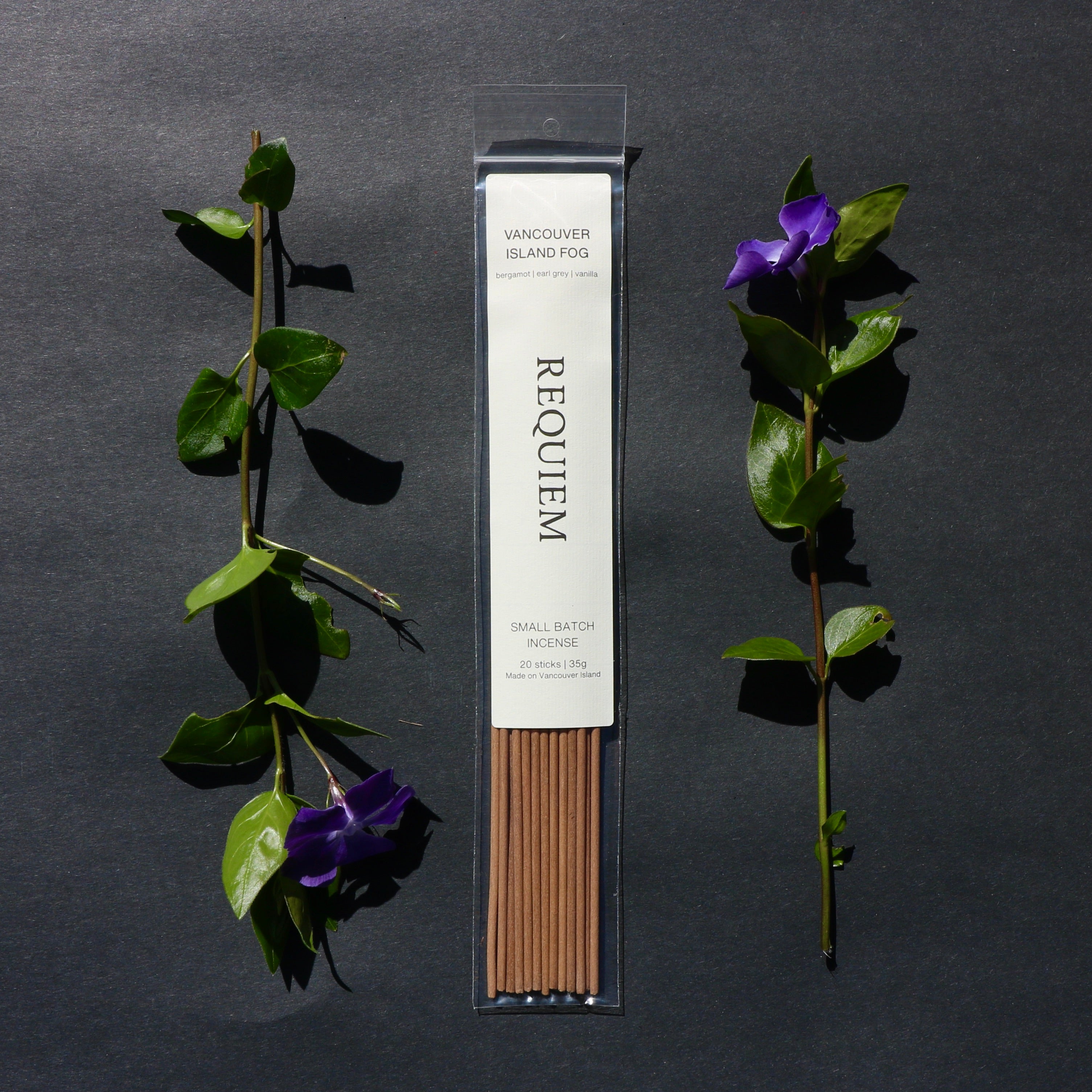 Requiem Incense Company Vancouver Island Fog incense sticks with green leaves and purple flowers on a dark background