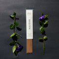 Requiem Incense Company Vanilla & Patchouli incense sticks with green leaves and purple flowers on a dark background