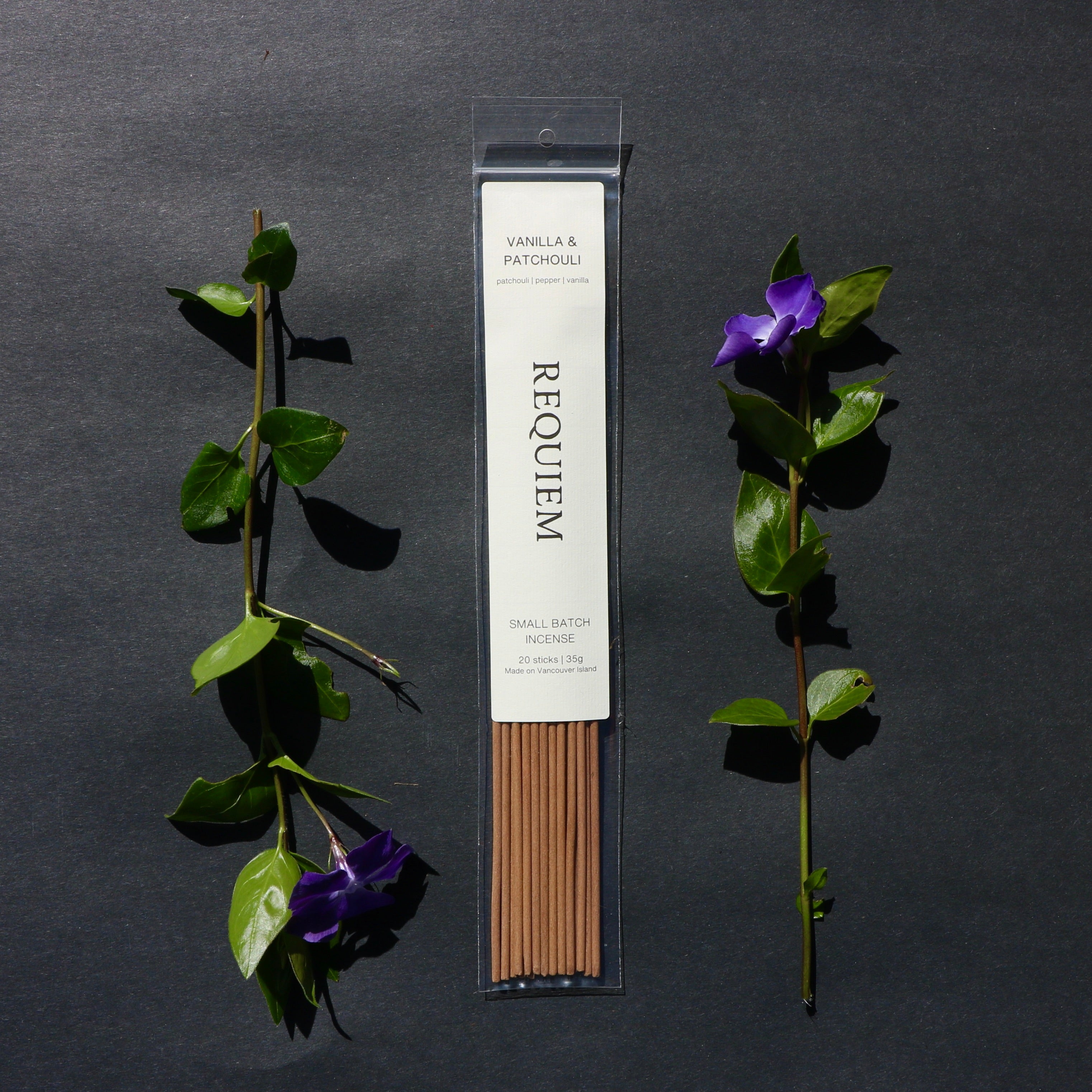 Requiem Incense Company Vanilla & Patchouli incense sticks with green leaves and purple flowers on a dark background